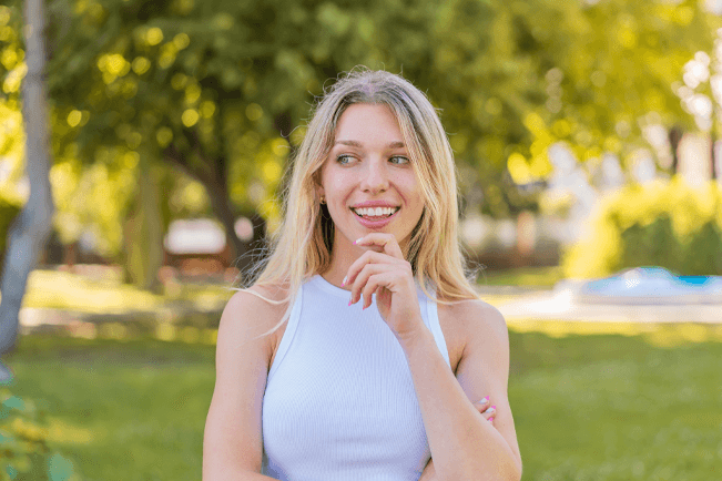 Vrouw denkt na en glimlacht buiten in de zon, symbool voor nieuwe ideeën en samenwerkingen