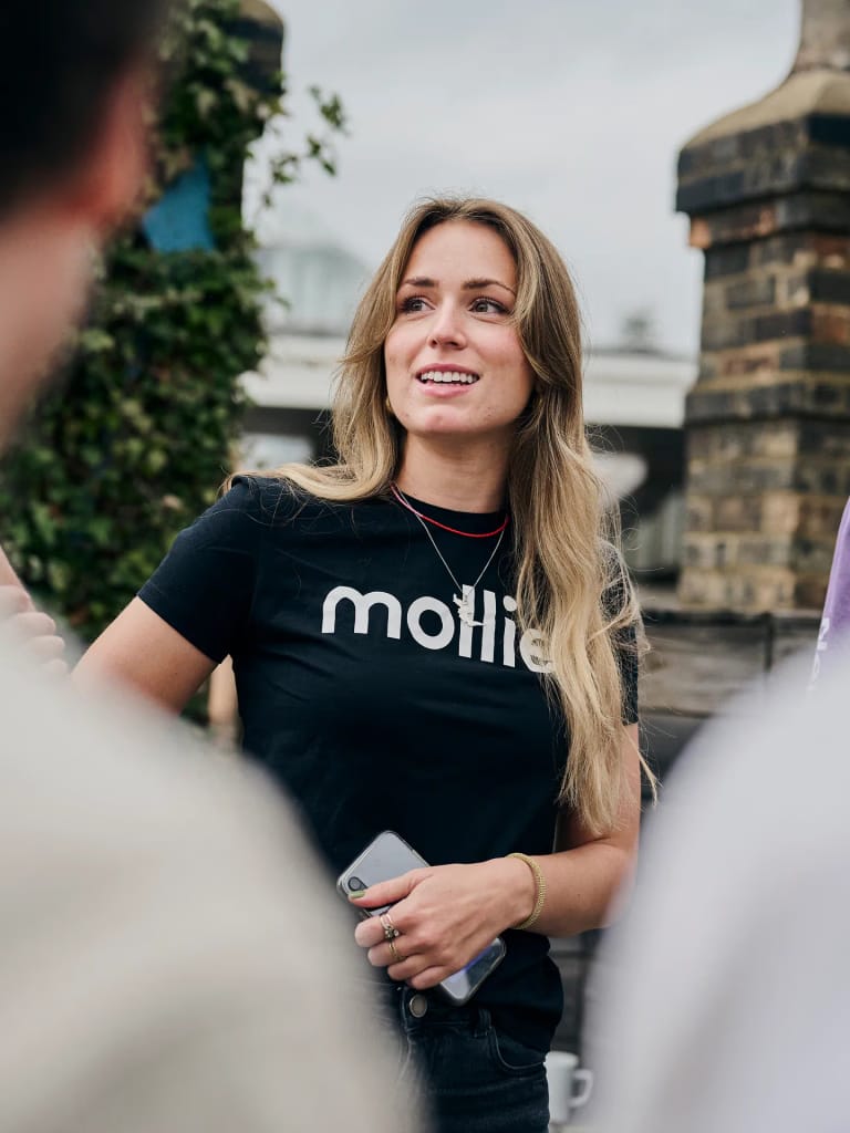 Vrouw draagt een zwart T-shirt met het logo van Mollie en houdt een smartphone vast — beeld dat symbool staat voor moderne online betalingen en samenwerking met Mollie.
