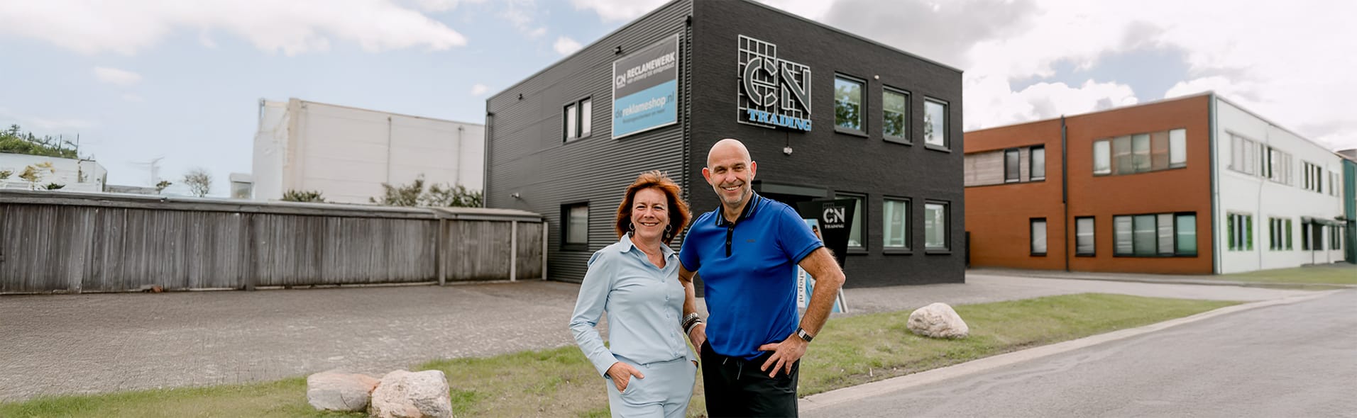 Twee ondernemers staan lachend voor een zwart kantoorpand met het logo van CN Trading.